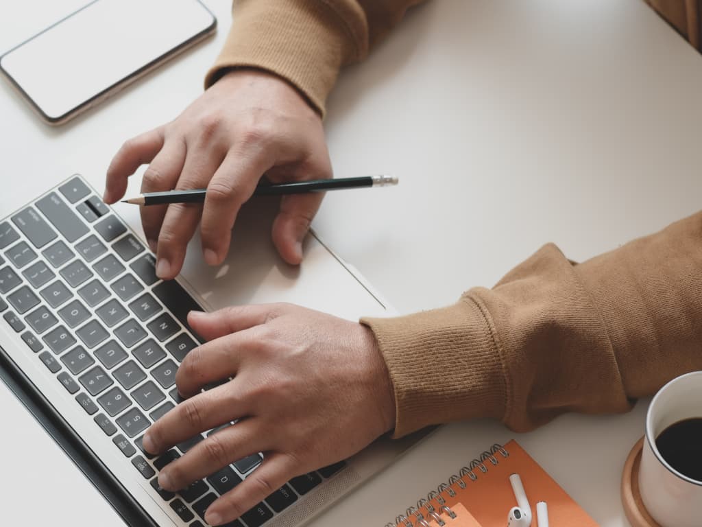 person on laptop with a coffee and a pencil in hand